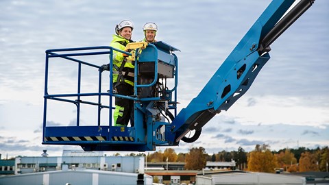 En man och en kvinna står i en lyftkorg i bomlift, högt upp i luften. 