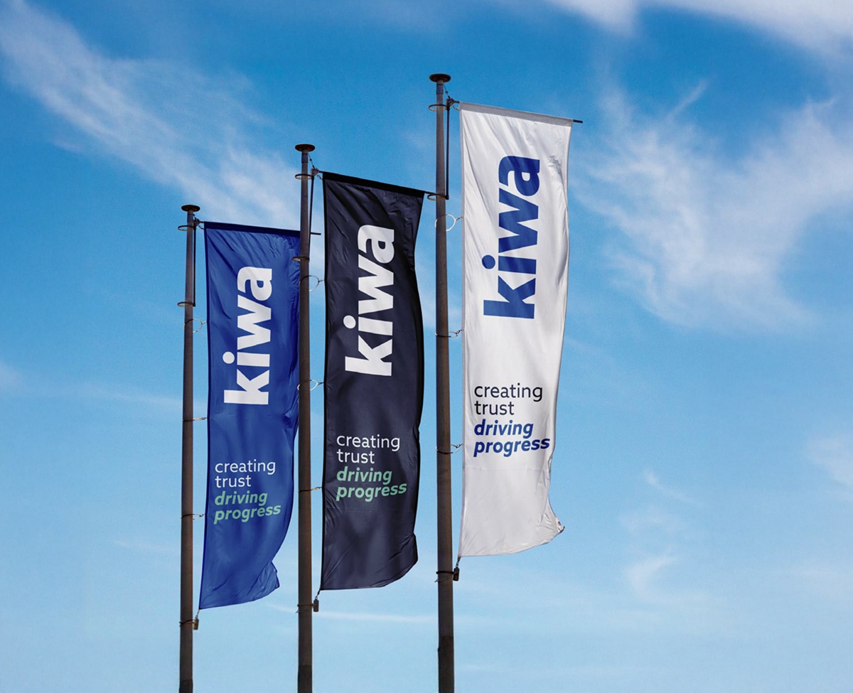 Three vertical flags with the word "Kiwa" and the slogan "creating trust driving progress" printed on them, against a blue sky background.