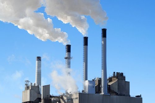 Industrial power plant with four smokestacks emitting white smoke against a clear blue sky