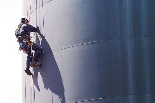 Industriklättrare, rope access, i sele som arbetar med att besiktiga en stor silotank.