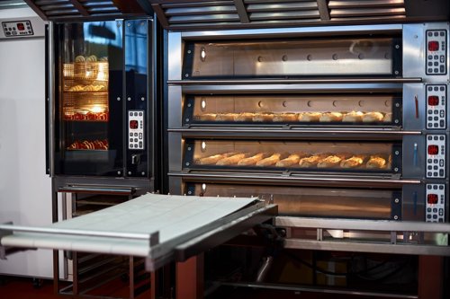 Bakkerijoven met meerdere lagen waarin broodjes worden gebakken, naast een aparte oven met brood zichtbaar.