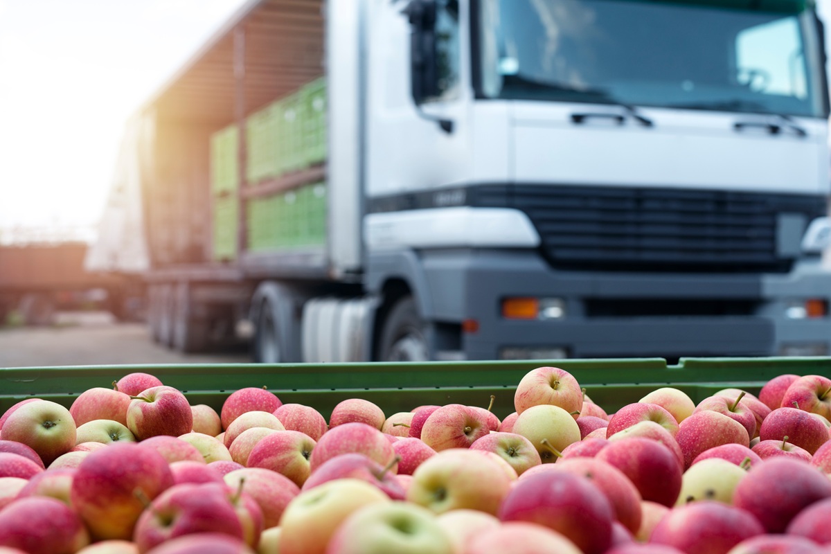 Rode en gele appels in een groene krat met een vrachtwagen op de achtergrond.
