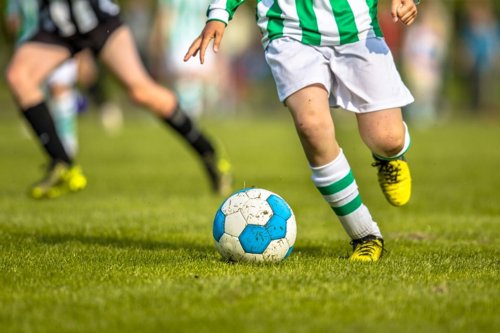 Voetballer op een grasveld, terwijl een tegenstander op de achtergrond te zien is.