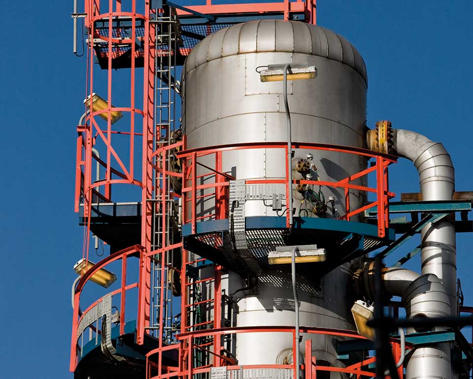 Industriell anläggning med stora silvertankar, röda metallräcken och rör mot blå himmel - gneom användning av databasen Matbas PED får du tillgång till information om vilka material som är godtagna under Tryckkärlsdirektivet PED.