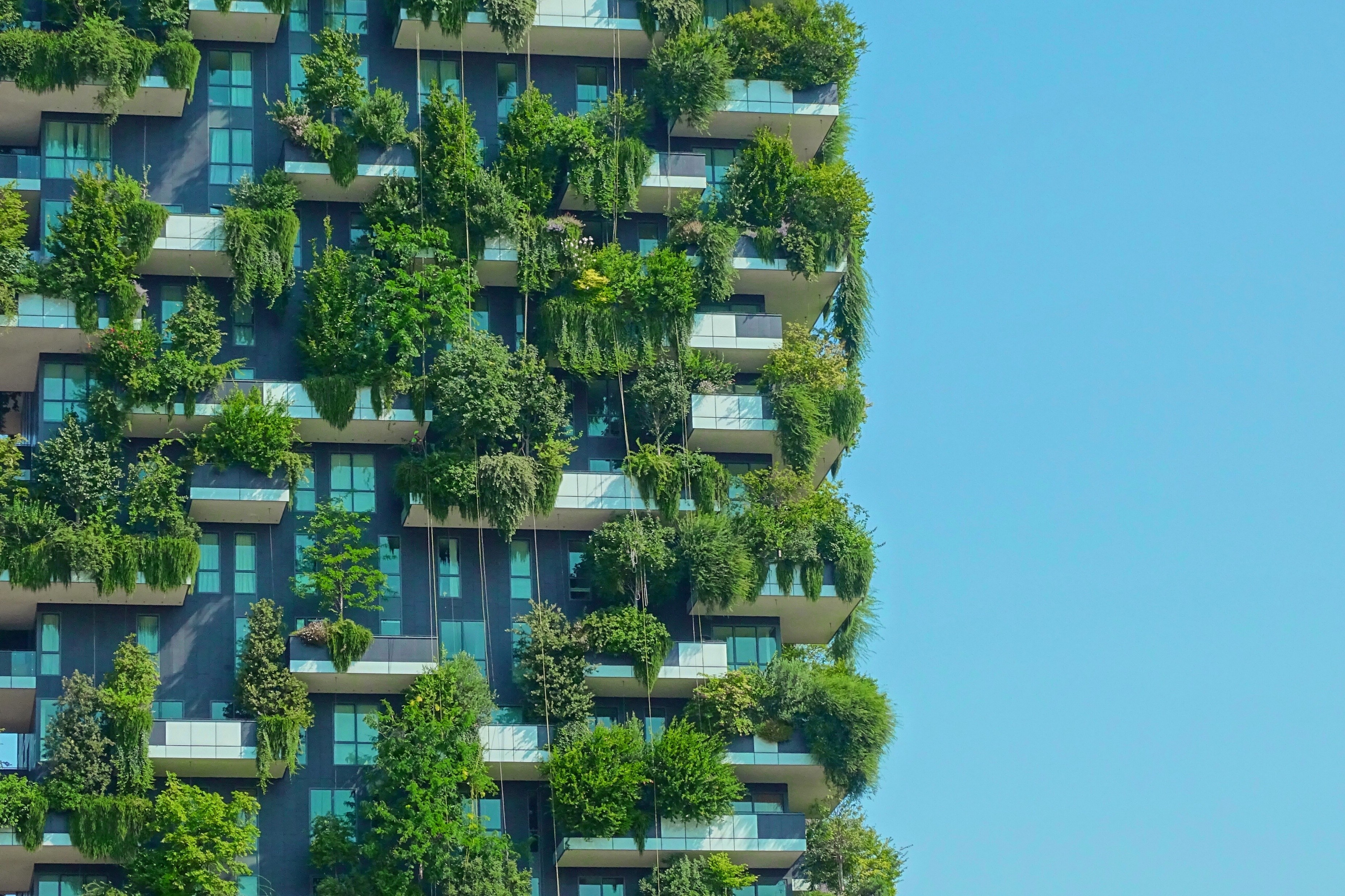 Modern high-rise building with lush vertical greenery and balconies against a clear blue sky