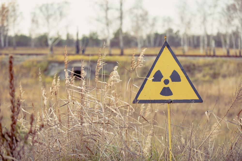 Yellow radiation warning sign in a grassy field with blurred trees in the background, indicating a potentially hazardous area
