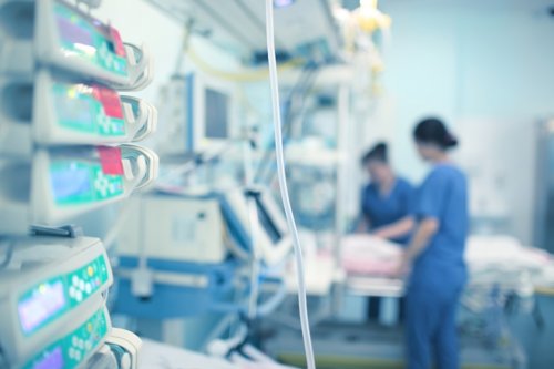 Hospital intensive care unit with medical equipment and two nurses attending a patient bed