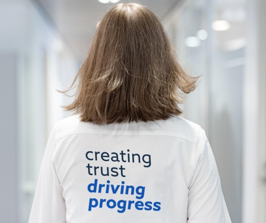 No muguras redzama sieviete baltā krekliņā ar uzrakstu “creating trust driving progress” koridorā.