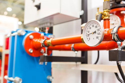 Red industrial pipe system with a pressure gauge displaying temperature in a mechanical room, indicating engineering and HVAC operations