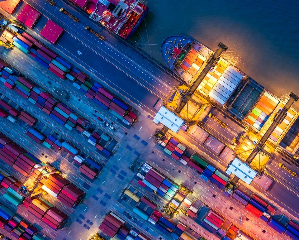 Aerial view of a busy shipping port with cargo containers and illuminated cranes at night, showcasing global trade activities.
