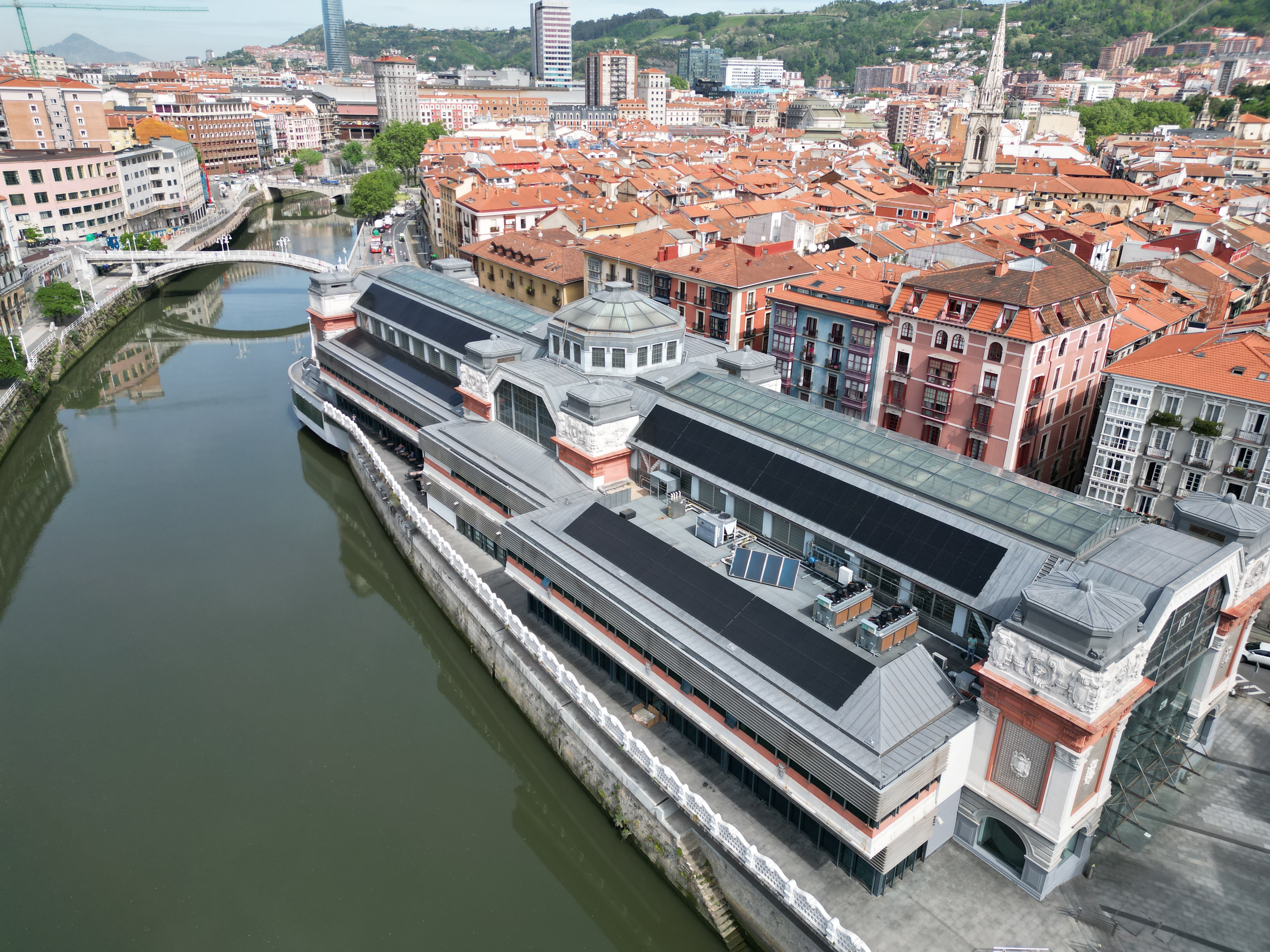 Aerial view of the Ribera Market in Bilbao, Spain, with the Nervion River running alongside and the cityscape with red-tiled roofs in the background