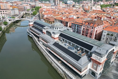 Aerial view of the Ribera Market in Bilbao, Spain, with the Nervion River running alongside and the cityscape with red-tiled roofs in the background