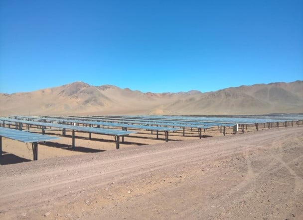 Solar panels in a desert landscape with mountains in the background under a clear blue sky
