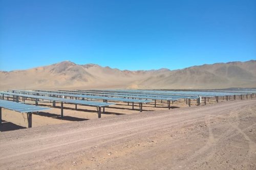 Solar panels in a desert landscape with mountains in the background under a clear blue sky
