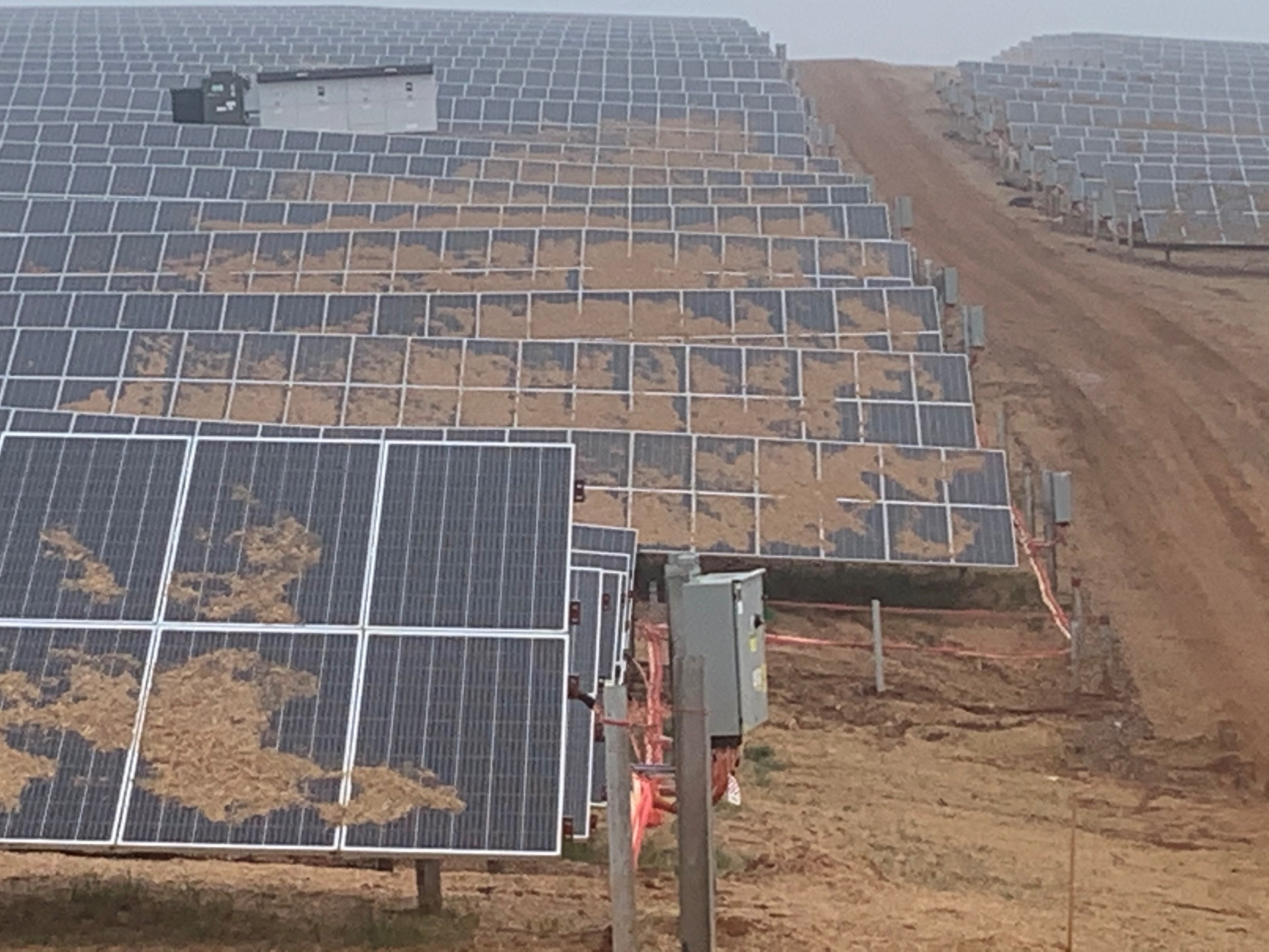 A large array of solar panels on a sloped, muddy terrain