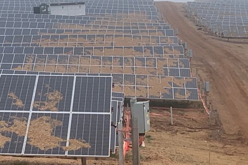 A large array of solar panels on a sloped, muddy terrain