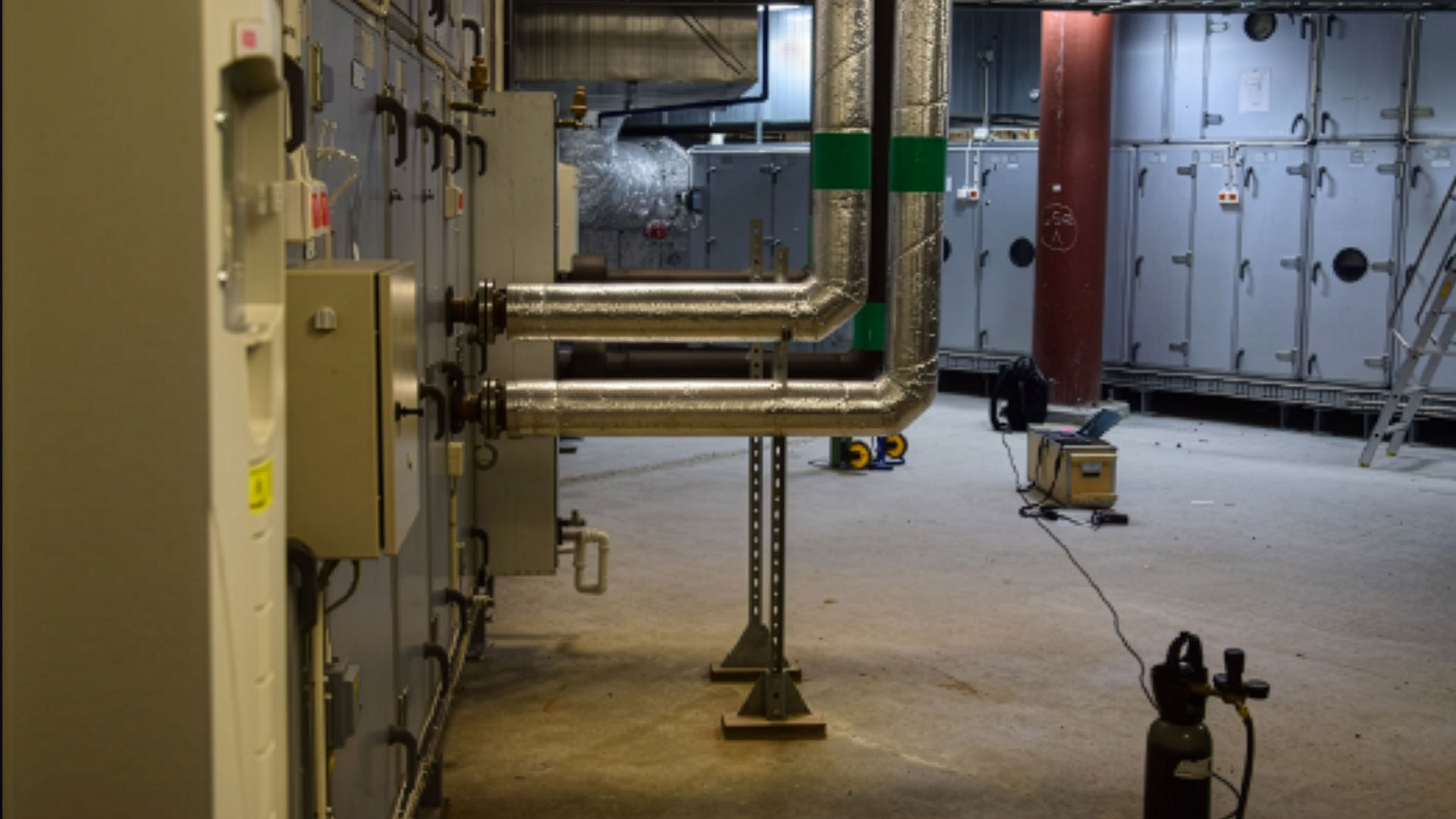 Spårgasmätning pågår i ett ventilationsrum med stora rör, isolerade kanaler och industriella aggregat i en byggnad.