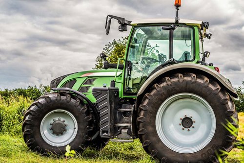 Grön traktor parkerad på en gräsbevuxen åker med molnig himmel i bakgrunden.
