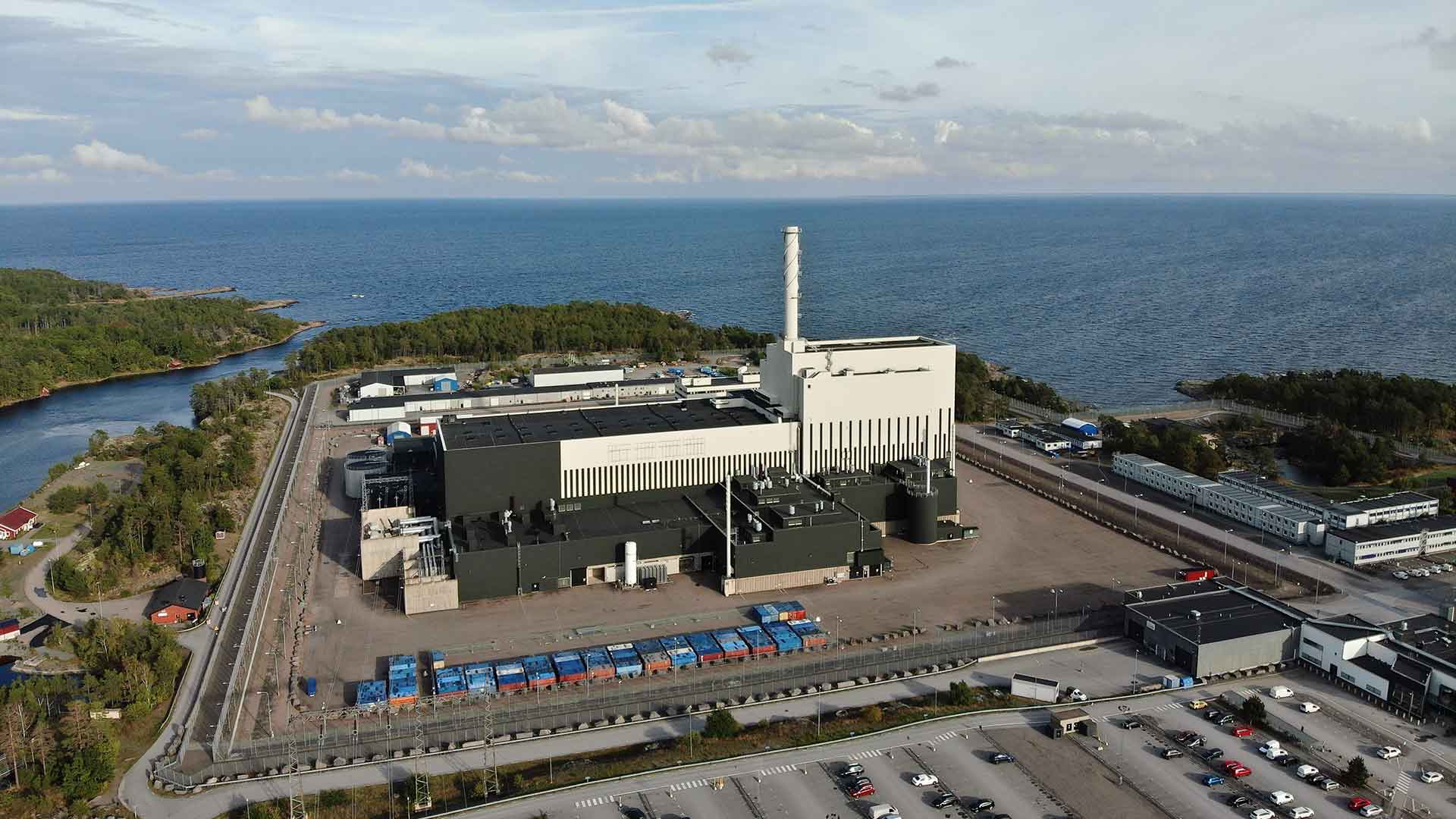 Aerial view of a large power plant by the sea, with an industrial area, a road, and a parking lot.